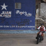 
              A woman rides her motorcycle past a campaign mural promoting the National Party presidential candidate Nasry Asfura known as "Papi a la orden",  in the Kennedy neighborhood of Tegucigalpa, Honduras, Friday, Nov. 26, 2021. Honduras will hold general election on Nov. 28. (AP Photo/Moises Castillo)
            