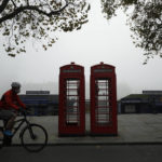 
              FILE - A cyclist wearing a face mask passes traditional red phone boxes, in London, on Nov. 5, 2020. Thousands of Britain’s iconic red phone boxes will be protected from removal under new rules, the telecoms regulator said Tuesday, Nov. 9, 2021. The public payphone boxes may appear obsolete relics to many in an age of smart mobile phones, but the telecoms regulator, Ofcom, said they can still be a “lifeline” for people in need. The regulator is proposing rules to prevent 5,000 phone boxes in areas with poor mobile coverage from being closed down. (AP Photo/Matt Dunham, File)
            