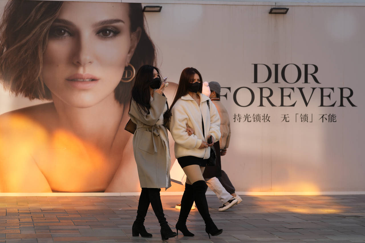 Women wearing masks walk past an ad for Dior at a mall in Beijing, China, Thursday, Nov. 25, 2021. ...
