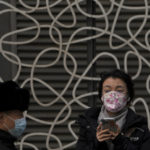 
              A woman wearing a face mask to protect from COVID-19 looks at a masked security guard patrolling at a commercial office building in Beijing, Sunday, Nov. 28, 2021. (AP Photo/Andy Wong)
            