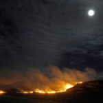 
              Grassland burns as the moon rises in the distance Thursday, Dec. 16, 2021, near Hays, Kan. The fire, which burned more than 365,850 acres and stretched across Ellis, Russell, Osborne and Rooks counties, was stoked by a storm that passed through the area Wednesday with high winds and gusts up to 90 mph. (AP Photo/Charlie Riedel)
            