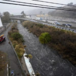 
              A San Diego Lifeguard River Team unit patrols along a flooded water way as it leads toward the San Diego River, Tuesday, Dec. 14, 2021, in San Diego. Rain is drenching Southern California as a powerful storm slides down the state, snarling traffic and raising the threat of mudslides in areas scarred by wildfires. (AP Photo/Gregory Bull)
            