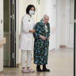 
              Dr. Saltanat Bekeeva, left, and 101-year-old patient Pelageya Poyarkova enter the hall to speak with media as she leaves the recovery ward for COVID-19 patients at the Federal Center for Brain and Neurotechnology in Moscow, Russia, Friday, Dec. 3, 2021. Russia has reported more than 9.7 million confirmed cases of COVID-19 in the pandemic and more than 270 thousands deaths, which experts believe could be undercounts. (AP Photo/Pavel Golovkin)
            