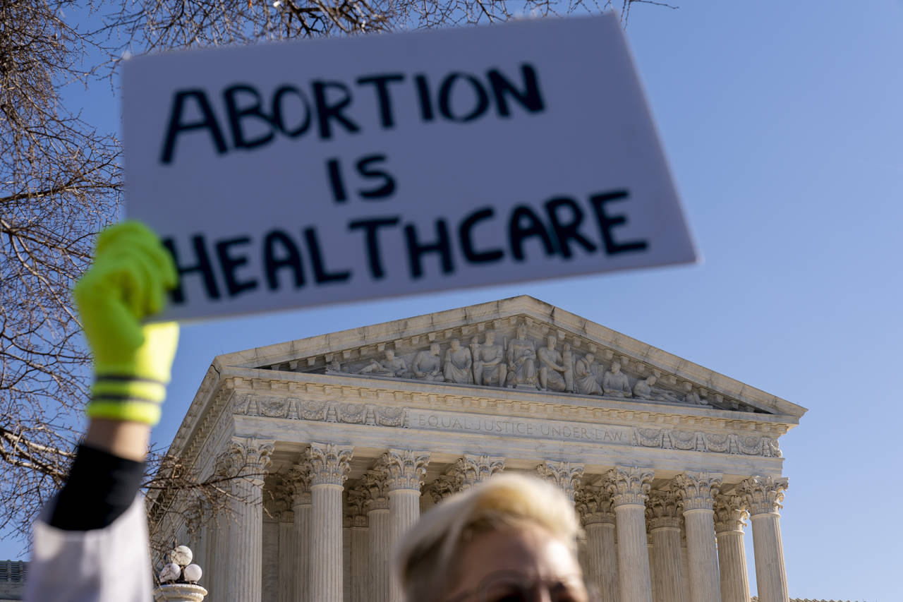 A woman in an doctors uniform holds a poster that reads "Abortion is Healthcare" as abortion rights...