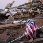 
              An American flag is draped over debris after a tornado in Dawson Springs, Ky., Sunday, Dec. 12, 2021. A monstrous tornado, carving a track that could rival the longest on record, ripped across the middle of the U.S. on Friday. (AP Photo/Michael Clubb)
            
