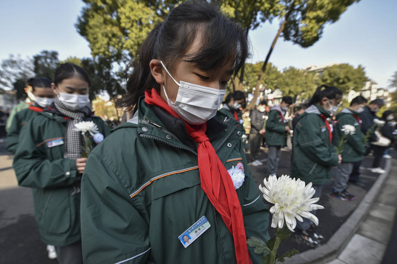 Students wearing face masks hold flowers mourn for the victims of the Nakjing Massacre at a mass bu...