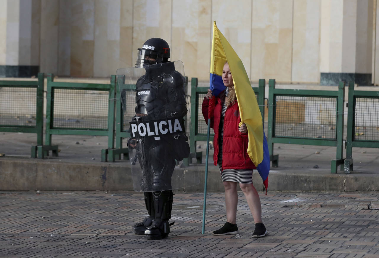 FILE - A woman holding a Colombian flag stands next to a police officer in riot gear during a prote...