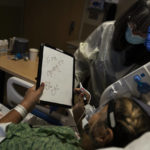 
              Mary Lou Samora, a 71-year-old COVID-19 patient, writes on a white board, "I'm going to be OK," while using the board to communicate with her long time friend, Becky Gonzalez, 67, at Providence Holy Cross Medical Center in Los Angeles, Friday, Dec. 17, 2021. (AP Photo/Jae C. Hong)
            