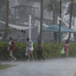 
              People scramble to get out of the heavy rain on Waikiki Beach, Monday, Dec. 6, 2021, in Honolulu. (AP Photo/Marco Garcia)
            