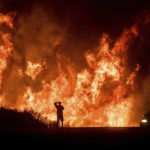 
              FILE - A motorists on Highway 101 watches flames from the Thomas fire leap above the roadway north of Ventura, Calif., on Dec. 6, 2017. Southern California Edison has reached an agreement with state regulators on Thursday, Dec. 16 2021, for more than half a billion dollars in penalties related to five wildfires, including the Thomas fire. (AP Photo/Noah Berger, File)
            