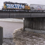
              A cargo train passes over a bridge where a submerged vehicle is wedged against the bridge's pillar in the surging Los Angeles River making it difficult for firefighters to access it on Tuesday, Dec. 14, 2021 in Los Angeles. The vehicle was spotted in the river before dawn. Rain is drenching Southern California as a powerful storm slides down the state, snarling traffic and raising the threat of mudslides in areas scarred by wildfires. (AP Photo/Damian Dovarganes)
            