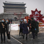 Visitors wearing face masks to help protect from the coronavirus gather to take souvenir photo with a decoration for the Beijing Winter Olympics Games on display at Qianmen Street, a popular tourist spot in Beijing, Sunday, Jan. 23, 2022. Chinese authorities have called on the public to stay where they are during the Lunar New Year instead of traveling to their hometowns for the year's most important family holiday. (AP Photo/Andy Wong)
