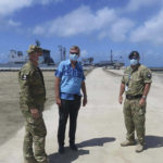 
              In this photo released by the New Zealand High Commission, Peter Lund, center, New Zealand’s acting high commissioner to Tonga, stands with military personnel at a wharf in Nuku'alofa, Tonga Friday, Jan. 21, 2022, after a New Zealand ship, seen in the background, arrived with water and other much-needed aid supplies. (New Zealand High Commission via AP)
            