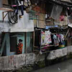 
              A woman carries her baby outside of her house in a low-income neighborhood next to a polluted city canal in Jakarta, Indonesia, Tuesday, Jan. 25, 2022. Indonesian parliament last week passed the state capital bill into law, giving green light to President Joko Widodo to start a $34 billion construction project this year to move the country's capital from the traffic-clogged, polluted and rapidly sinking Jakarta on the main island of Java to jungle-clad Borneo island amid public skepticism. (AP Photo/Dita Alangkara)
            