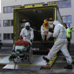 
              FILE - Health care workers transport a COVID-19 patient, in Ceska Lipa, Czech Republic, Thursday, March 18, 2021. Czech Republic's Health Minister Vlastimil Valek said Friday Jan. 14, 2022 that the new Czech government will allow some people who have been tested positive for the coronavirus to keep working, an extraordinary measure to ease possible staff shortages caused by an anticipated surge of the omicron variant. The measure, which was used during the previous coronavirus waves, would only apply for workers at the health care system and in nursing homes who have no symptoms of COVID-19. (AP Photo/Petr David Josek, File)
            