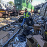
              Contractor worker Adam Rodriguez picks up vehicle tires from the shredded boxes and packages along a section of the Union Pacific train tracks in downtown Los Angeles Friday, Jan. 14, 2022. Thieves have been raiding cargo containers aboard trains nearing downtown Los Angeles for months, leaving the tracks blanketed with discarded packages. The sea of debris left behind included items that the thieves apparently didn't think were valuable enough to take, CBSLA reported Thursday. (AP Photo/Ringo H.W. Chiu)
            
