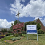 
              This photo provided by the Rev. Lucy Robbins shows a "For Sale" sign in front of the Biltmore United Methodist Church in Asheville, N.C. in July 2021. Already financially strapped because of shrinking membership and a struggling preschool, the congregation was dealt a crushing blow by the coronavirus. Attendance plummeted, with many staying home or switching to other churches that stayed open the whole time. Gone, too, is the revenue the church formerly got from renting its space for events and meetings. (Rev. Lucy Robbins via AP)
            