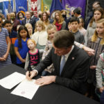 
              FILE - Virginia Gov. Glenn Youngkin, signs an executive order establishing K through 12 lab schools while surrounded by children and educators at the Capitol, Jan. 27, 2022, in Richmond, Va. In his opening days, the new governor issued executive orders methodically ticking off his top campaign promises that effectively banned classroom mask mandates, aimed to restrict how students are taught about racism, approved an investigation into a wealthy suburban Washington school district that's become a national symbol for battles over so-called parents rights and attempted to scrap a carbon-limiting initiative meant to combat climate change. (AP Photo/Steve Helber, File)
            