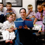 
              This undated photo provided by Robert Krause shows his daughter, Sasha Krause, center, reading a book to children in Farmington, New Mexico. Krause was killed in early 2019. Air Force Airman Mark Gooch was found guilty of first-degree murder and will be sentenced Jan. 19, 2022. (Family Photo/Robert Krause via AP)
            