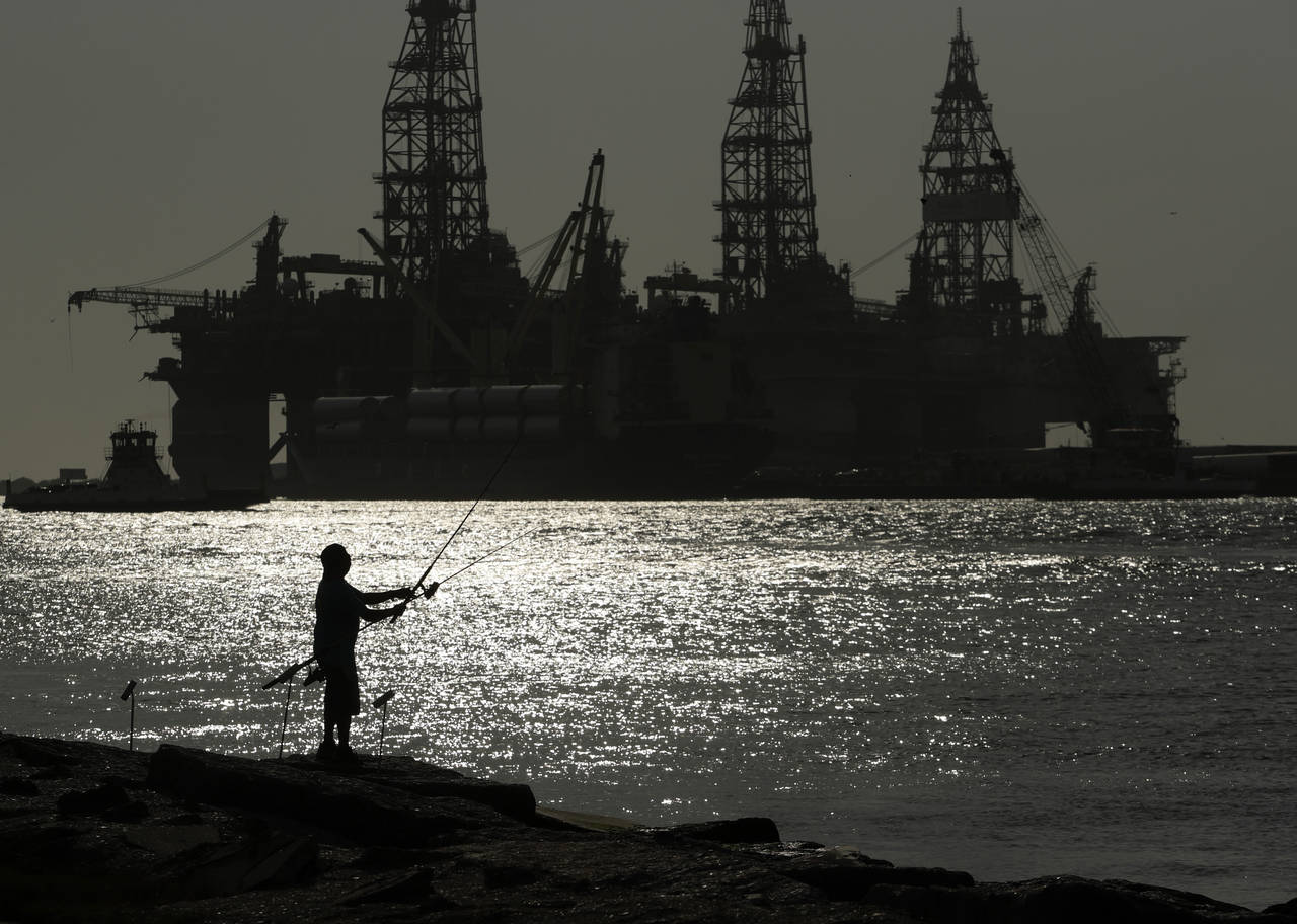 FILE - A man wears a face mark as he fishes near docked oil drilling platforms, on May 8, 2020, in ...