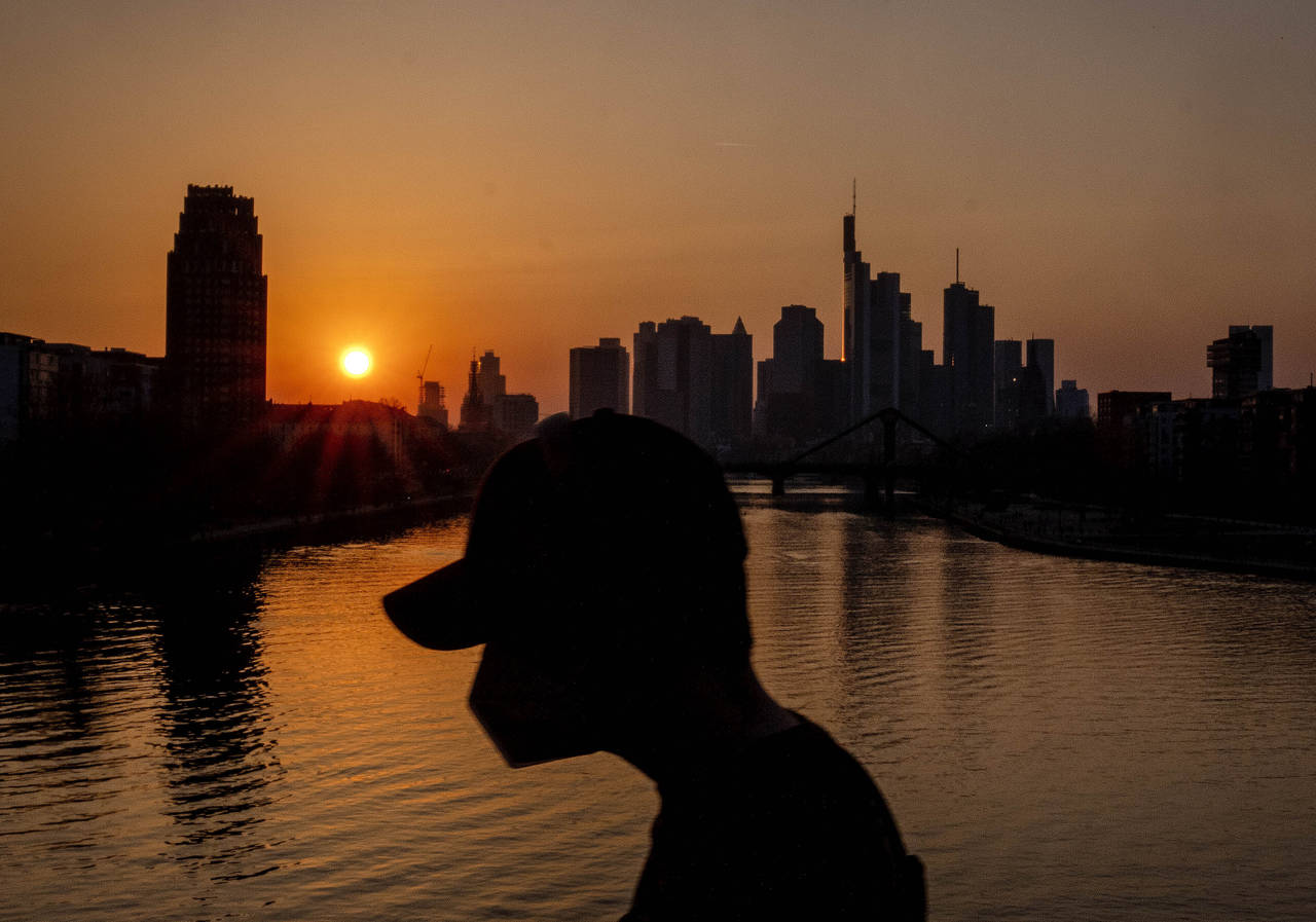 A man wears a face mask as he walks on a bridge over the river Main as the sun sets in Frankfurt, G...