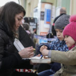 
              A woman and her children have a meal after fleeing the war from neighboring Ukraine at a railway station in Przemysl, Poland, on Friday, March 25, 2022. (AP Photo/Sergei Grits)
            