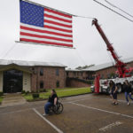 
              FILE - Attendees of the funeral services for Louisiana State Police Master Trooper Chris Hollingsworth, walk past a suspended American flag, Friday, Sept. 25, 2020, in West Monroe, La. Hollingsworth, killed in a car crash hours after he was told he would be fired for his role in the death of a Black man, was buried with honors Friday at a ceremony that authorities sought to keep secret out of concerns it would attract a mass protest. (AP Photo/Rogelio V. Solis, File)
            