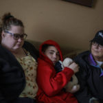 
              Cathie Quackenbush, right, sits on the couch with her children, Landon, 13, and Macy Sweeters, at their home in Springfield, Mo., Tuesday, March 22, 2022. Larry Quackenbush, 60, was the glue that held his family together. After his wife, Cathie, suffered brain damage in a car accident more than 20 years ago, he became the primary cook, carpooler and caregiver, while continuing to work. When Landon, came home from summer camp sick with COVID, Quackenbush stepped up again. "Even when he started feeling sick, he kept taking care of everybody," Sweeters says. (AP Photo/David Goldman)
            