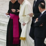 
              Pope Francis, second from left, leans on Monsignor Leonardo Sapienza, left, as he walks down the steps at the end of his weekly general audience in the Paul VI Hall, at the Vatican, Wednesday, April 6, 2022. (AP Photo/Alessandra Tarantino)
            