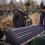 
              Vova, 10, looks at the coffin carrying body of his mother, Maryna, as his father, Ivan Drahun, hugs him during her funeral in Bucha, on the outskirts of Kyiv, on Wednesday, April 20, 2022. Vova's mother died while they sheltered in a cold basement for more than a month during the Russian military's occupation. (AP Photo/Emilio Morenatti)
            