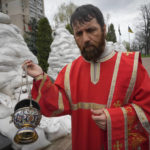 
              An Orthodox priest holds a commemorative ceremony to pay respect to the Chernobyl firefighters at a memorial in capital Kyiv, Ukraine, Tuesday, April 26, 2022. Firefighter sculptures at rear are covered with bags to protect against the Russian shelling. April 26 marks the 36th anniversary of the Chernobyl nuclear disaster. A reactor at the Chernobyl nuclear power plant exploded on April 26, 1986, leading to an explosion and the subsequent fire spewed a radioactive plume over much of northern Europe. (AP Photo/Efrem Lukatsky)
            