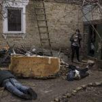 
              Ira Gavriluk holds her cat as she walks next to the bodies of her husband, brother, and another man, who were killed outside her home in Bucha, on the outskirts of Kyiv, Ukraine, Monday, April 4, 2022. Russia is facing a fresh wave of condemnation after evidence emerged of what appeared to be deliberate killings of civilians in Ukraine. (AP Photo/Felipe Dana)
            