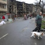 
              A man with a dog walks in a street along damaged during a heavy fighting apartment buildings in an area controlled by Russian-backed separatist forces in Mariupol, Ukraine, Tuesday, April 19, 2022. Taking Mariupol would deprive Ukraine of a vital port and complete a land bridge between Russia and the Crimean Peninsula, seized from Ukraine from 2014. (AP Photo/Alexei Alexandrov)
            