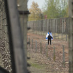 
              A man walks covered by Israeli flag at the Auschwitz Nazi concentration camp after the March of the Living annual observance that was not held for two years due to the global COVID-19 pandemic, in Oswiecim, Poland, Thursday, April 28, 2022. Only eight survivors and some 2,500 young Jews and non-Jews are taking part in the annual march that is scaled down this year because of the war in neighboring Ukraine that is fighting Russia's invasion. (AP Photo/Czarek Sokolowski)
            