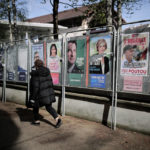
              A woman walks past presidential campaign posters during the first round of the French presidential election in Saint-Denis, outside Paris, Sunday, April 10, 2022. The polls opened at 8am in France for the first round of its presidential election where up to 48 million eligible French voters will be choosing between 12 candidates. (AP Photo/Lewis Joly)
            