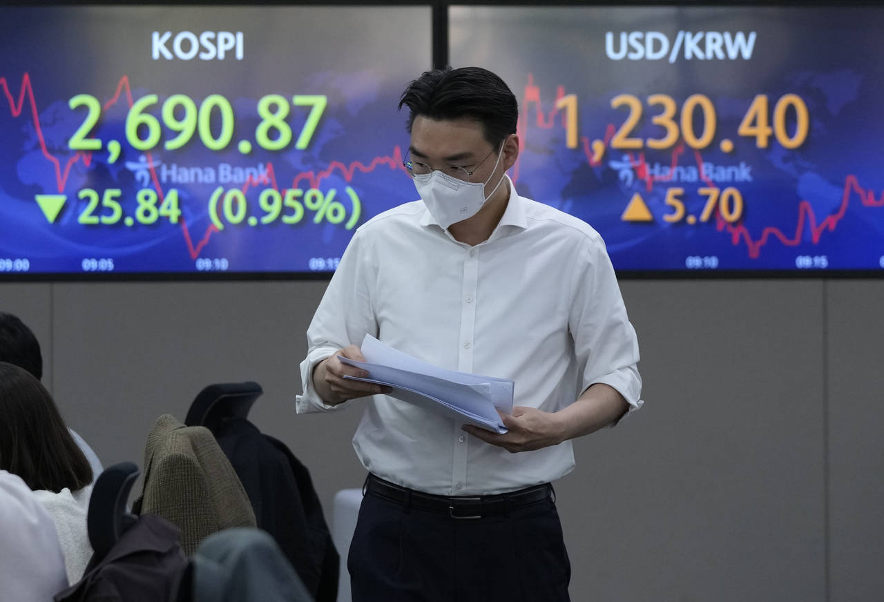 A currency trader passes by screens showing the Korea Composite Stock Price Index (KOSPI), left, an...