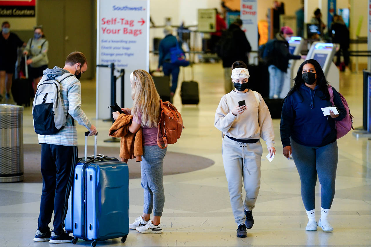 FILE - Travelers wearing protective masks as a precaution against the spread of the coronavirus mov...