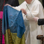 
              Pope Francis shows a flag that he said was sent to him from Bucha, Ukraine, during his weekly general audience in the Paul VI Hall, at the Vatican, Wednesday, April 6, 2022. (AP Photo/Alessandra Tarantino)
            