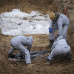 
              Men wearing protective gear exhume the bodies of civilians killed during the Russian occupation in Bucha, on the outskirts of Kyiv, Ukraine, Wednesday, April 13, 2022. Dozens of bodies of civilians executed by the Russian troops have been exhumed already from the mass grave. (AP Photo/Efrem Lukatsky)
            