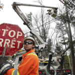 
              FILE - Canadian lineman Noah Clowater holds a bilingual stop sign while directing traffic while his coworkers restore power, Nov. 1, 2017, in Yarmouth, Maine. Weather disasters fueled by climate change now roll across the U.S. year-round, battering the nation's aging electric grid. (AP Photo/Robert F. Bukaty, File)
            