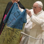 
              Pope Francis shows a flag that was brought to him from Bucha, Ukraine, during his weekly general audience in the Paul VI Hall, at the Vatican, Wednesday, April 6, 2022. (AP Photo/Alessandra Tarantino)
            