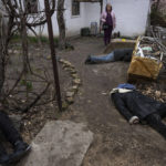 
              FILE - A woman stands next to three people killed in the courtyard of a house in Bucha, on the outskirts of Kyiv, Ukraine, Tuesday, April 5, 2022. (AP Photo/Rodrigo Abd, File)
            
