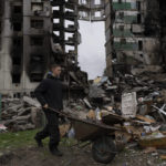
              A young man pushes a wheelbarrow in front of a destroyed apartment building in the town of Borodyanka, Ukraine, on Sunday, April 10, 2022. (AP Photo/Petros Giannakouris)
            