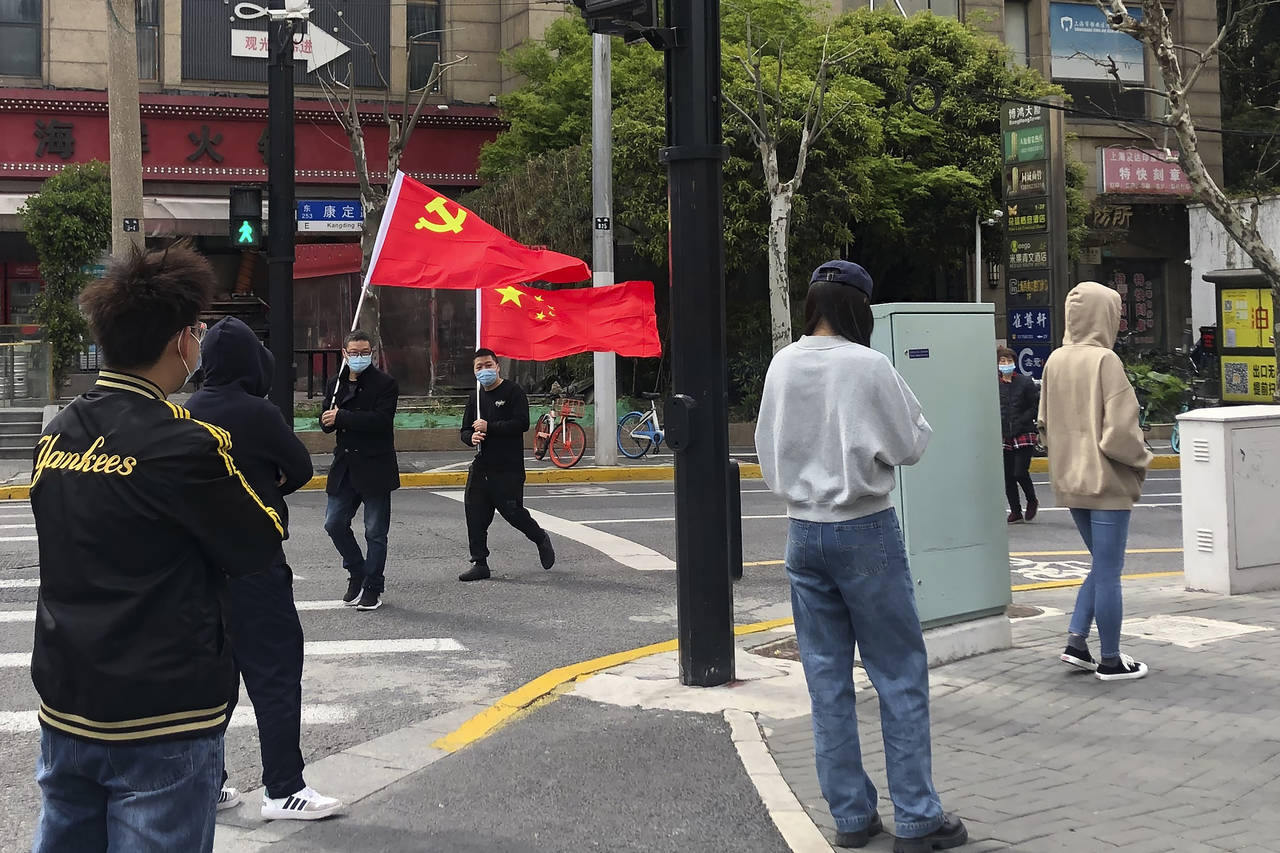 FILE - Residents hold up the Communist Party flag and the Chinese national flag as others prepare t...