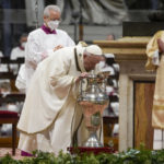 
              Pope Francis breaths inside a jar containing oil during a Chrism Mass inside St. Peter's Basilica, at the Vatican, Thursday, April 14, 2022. During the mass the Pontiff blesses a token amount of oil that will be used to administer the sacraments for the year. (AP Photo/Gregorio Borgia)
            