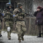 
              A woman looks at Ukrainian servicemen walking in the formerly Russian-occupied Kyiv suburb of Bucha, Ukraine, Saturday, April 2, 2022. As Russian forces pull back from Ukraine's capital region, retreating troops are creating a "catastrophic" situation for civilians by leaving mines around homes, abandoned equipment and "even the bodies of those killed," President Volodymyr Zelenskyy warned Saturday.(AP Photo/Vadim Ghirda)
            