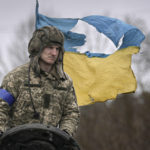 
              A Ukrainian serviceman is backdropped by his country's flag while standing on a tank, outside Kyiv, Ukraine, Saturday, April 2, 2022. As Russian forces pull back from Ukraine's capital region, retreating troops are creating a "catastrophic" situation for civilians by leaving mines around homes, abandoned equipment and "even the bodies of those killed," President Volodymyr Zelenskyy warned Saturday.(AP Photo/Vadim Ghirda)
            