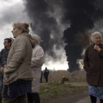 
              People stay in a yard as smoke rises in the air in the background after shelling in Odessa, Ukraine, Sunday, April 3, 2022. (AP Photo/Petros Giannakouris)
            