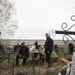
              Vlad Minchenko, second left, smokes a cigarette in the graveyard in Bucha, Ukraine, Tuesday, April 19, 2022. Minchenko wakes every day with trembling hands. For hours, until it eases, he can't message on his phone or even consider his previous work of making art or tattoos. But he can continue to retrieve bodies, scores of bodies, around the Ukrainian town of Bucha as part of a task that continues more than three weeks after Russian forces withdrew. (AP Photo/Evgeniy Maloletka)
            
