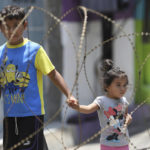 
              Children walk behind concertina wire as soldiers guard the entrances of the San Jose del Pino Community in Santa Tecla, El Salvador, Wednesday, April 6, 2022, during the government's unprecedented crackdown on gangs. El Salvador's congress, pushing further in the government's crackdown, has authorized prison sentences of 10 to 15 years for news media that reproduce or disseminate messages from the gangs, alarming press freedom groups. (AP Photo/Salvador Melendez)
            